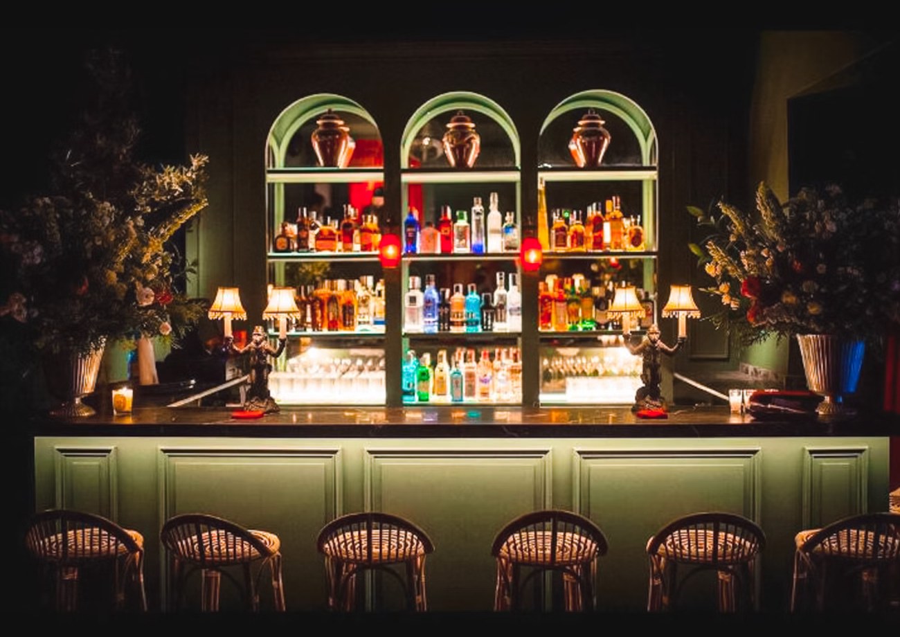 La barra: tres arcos verdes con botellas iluminadas, lámparas de monos y taburetes de ratán